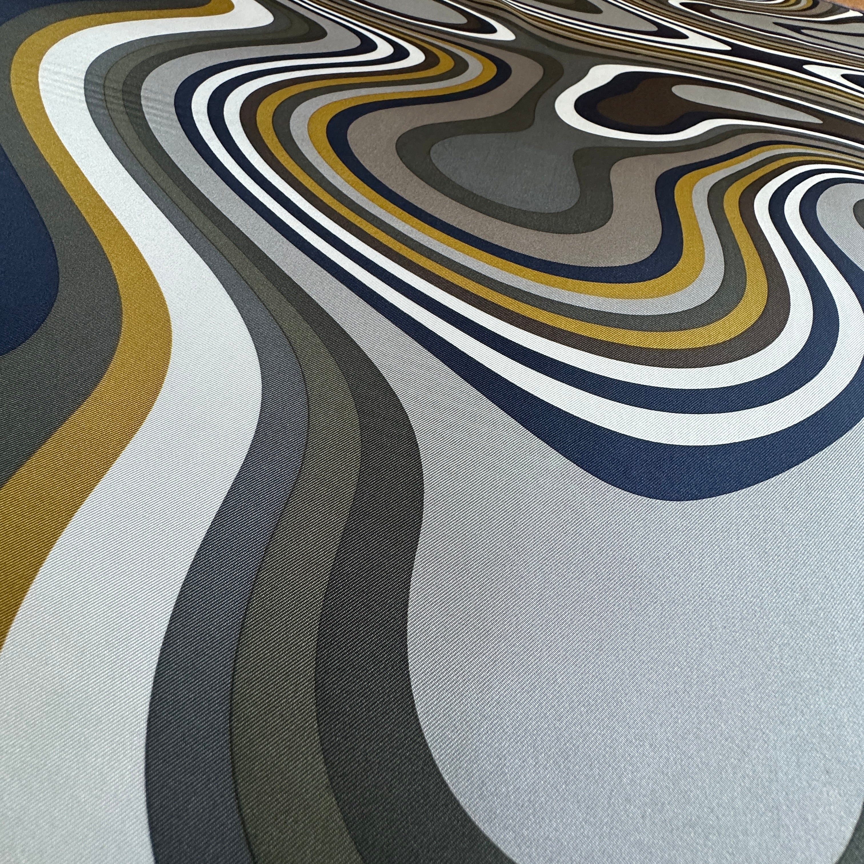Gros plan artistique montrant la fluidité de la soie et le mouvement hypnotique des lignes topographiques du design.