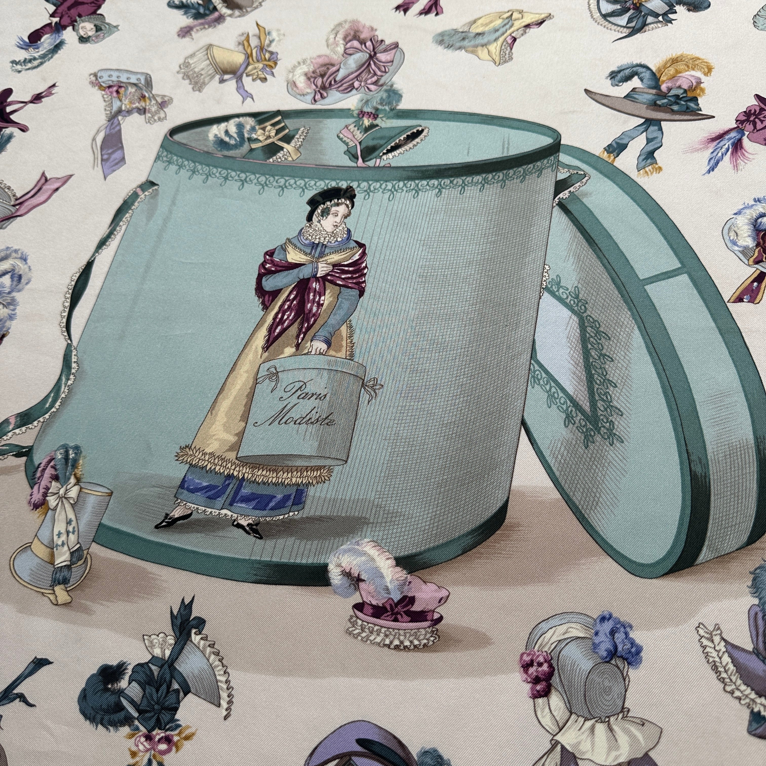 Gros plan sur la texture de la boîte à chapeaux bleue centrale et la finesse des traits de Hugo Grygkar.